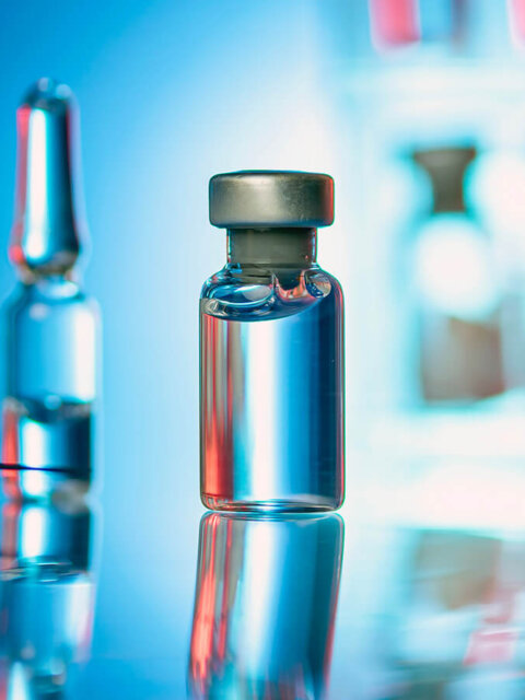 Close up shot of glass bottles, ampules and syringe with needle.
